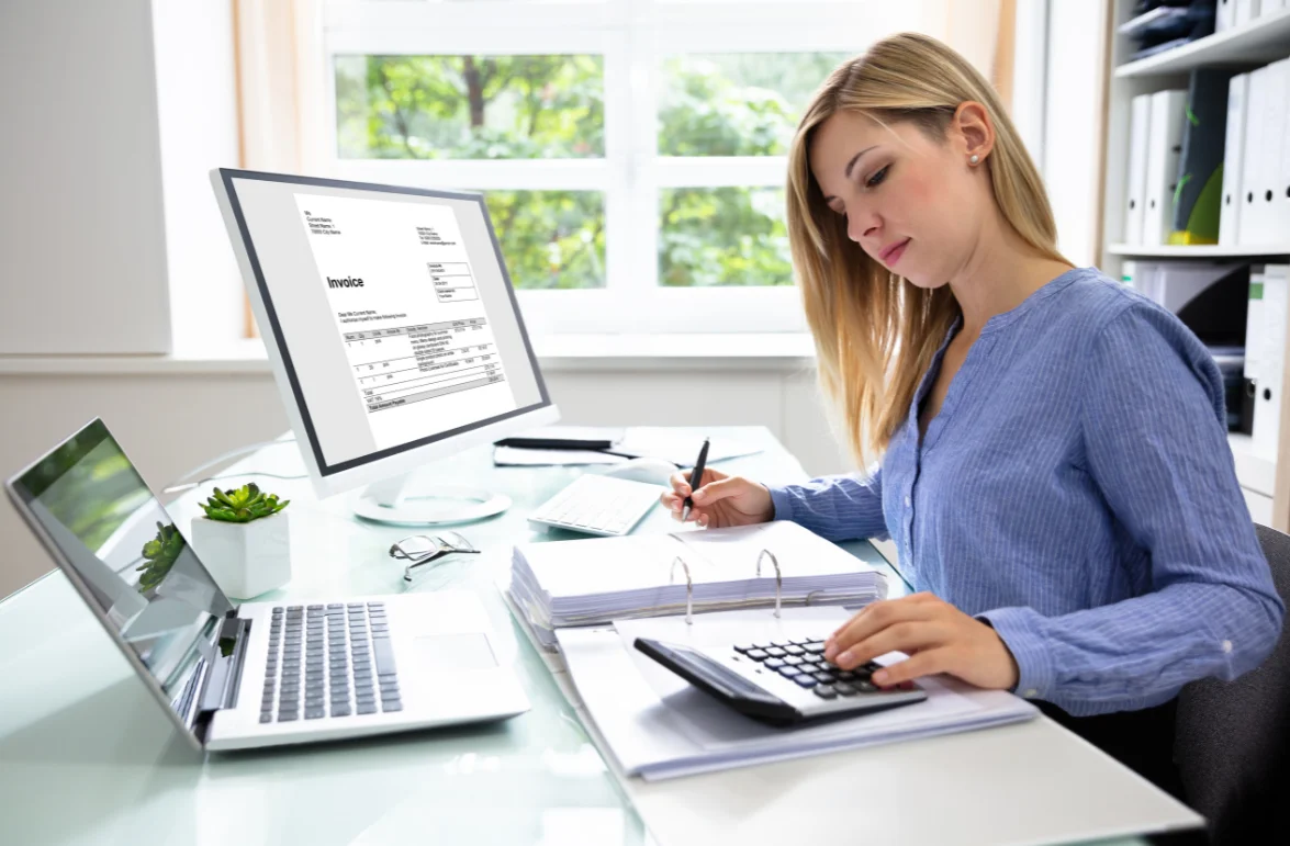 A business professional calculates tax credits, using a calculator and reviewing an invoice on the computer screen for accuracy.